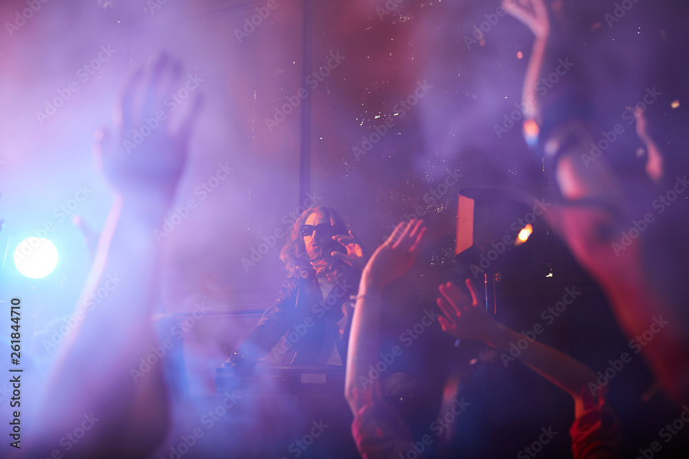 Obraz premium Popular handsome young dj playing record turntables and gesturing hands while interacting with crows at party in smoky nightclub