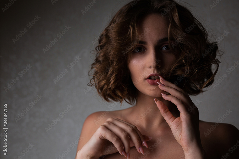 Closeup portrait of magnificent brunette model with curly hair posing in the shadows. Empty space