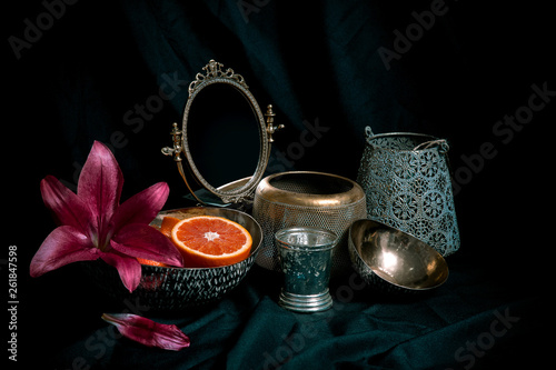 Fine art style low key still life with antique decor items on dark background. Composition of vases, flowers, mirror, orange with space for design. image for decorative shop photo