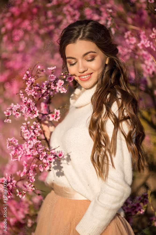 Pretty smiling girl posing near blossom tree with pink flowers.