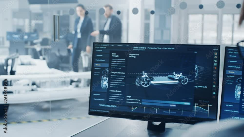 Professional Engineer Works on a Computer with a 3D CAD Software and Tests the Electric Car Chassis Prototype with Wheels, Batteries and Engine Standing in a High Tech Development Laboratory.