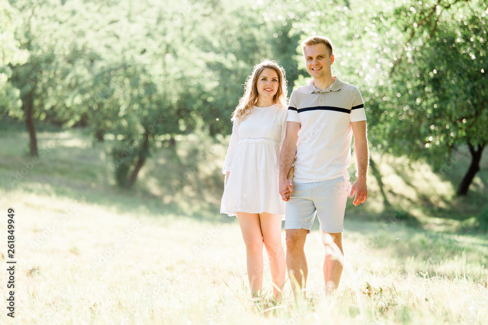 Young pretty couple in love walking in park. Handsome cheerful blonde girl in white dress hugging her boyfriend. Man and woman having fun outdoors Young pretty couple in love walking in park. Handsome cheerful blonde girl in white dress hugging her boyfriend. Man and woman having fun outdoors