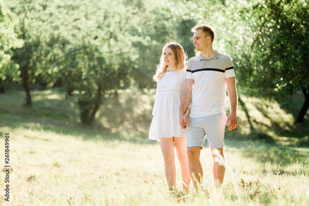 Young pretty couple in love walking in park. Handsome cheerful blonde girl in white dress hugging her boyfriend. Man and woman having fun outdoors Young pretty couple in love walking in park. Handsome cheerful blonde girl in white dress hugging her boyfriend. Man and woman having fun outdoors