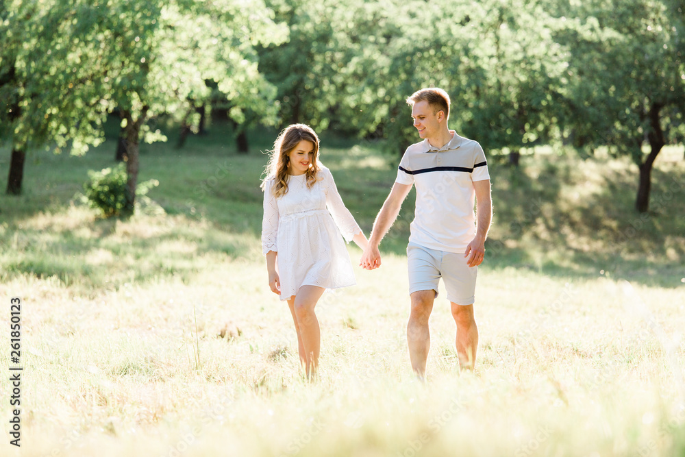 Young pretty couple in love walking in park. Handsome cheerful blonde girl in white dress hugging her boyfriend. Man and woman having fun outdoors Young pretty couple in love walking in park. Handsome cheerful blonde girl in white dress hugging her boyfriend. Man and woman having fun outdoors