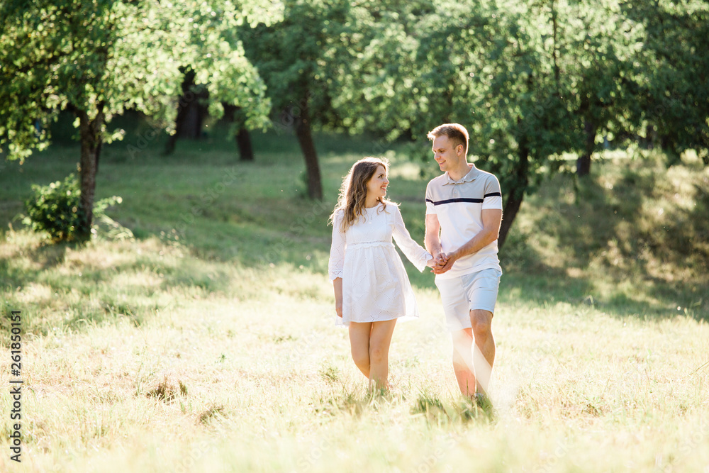 Young pretty couple in love walking  in park. Handsome cheerful blonde girl in white dress hugging her boyfriend. Man and woman having fun outdoors