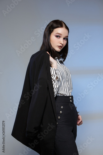 Young beautiful female fashion model in a business stylish suit on a rerom background. Holds a stack of papers and a pen.
