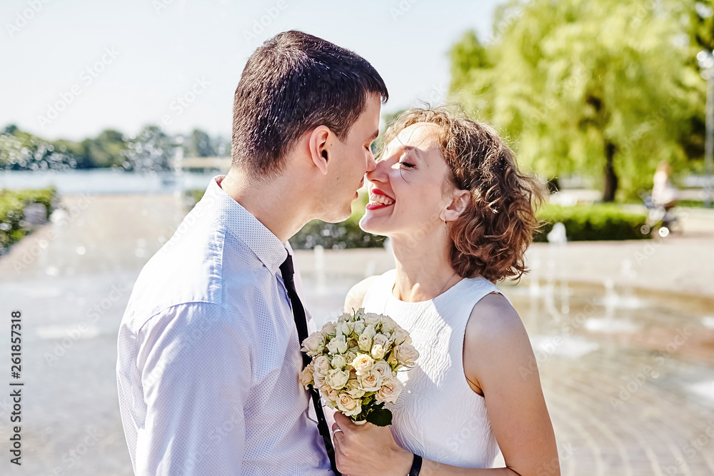 Happy young couple in love. Bride and groom hug in the park near the fountain. Woman laughing outdoor. Summer sunny day Happy young couple in love. Bride and groom hug in the park near the fountain. Woman laughing outdoor. Summer sunny day