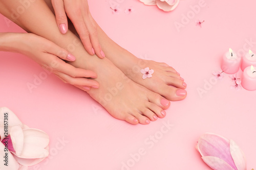 Beautiful shoot of female hands and feet on pink background surrounded by magnolia pink flowers.
