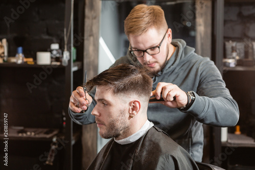 Hair cutting with metal scissors. Master cuts hair and beard of men in the barbershop, hairdresser makes hairstyle for a young man