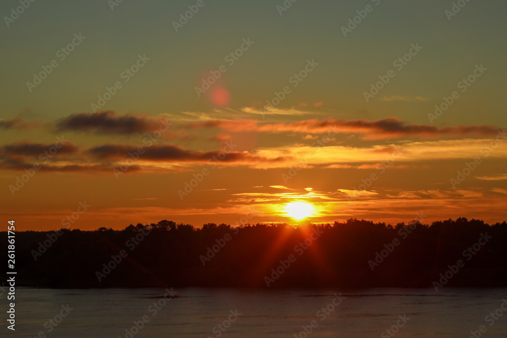 Naklejka premium Beautiful deep morning dawn with highlights in the orange rays of the summer sun on a river Volga with sun glare.. Toned in orange colour and backlit.