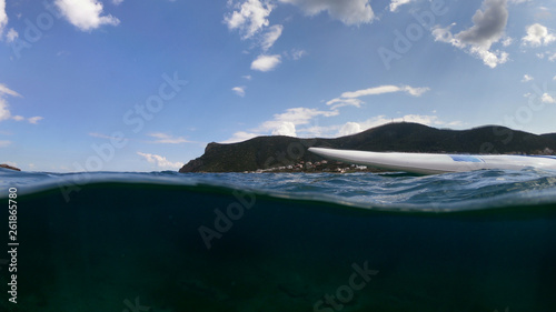Underwater sea level photo of unidentified man in a paddle surf board known as Sup surfing in turquoise clear waters and beautiful blue cloudy sky