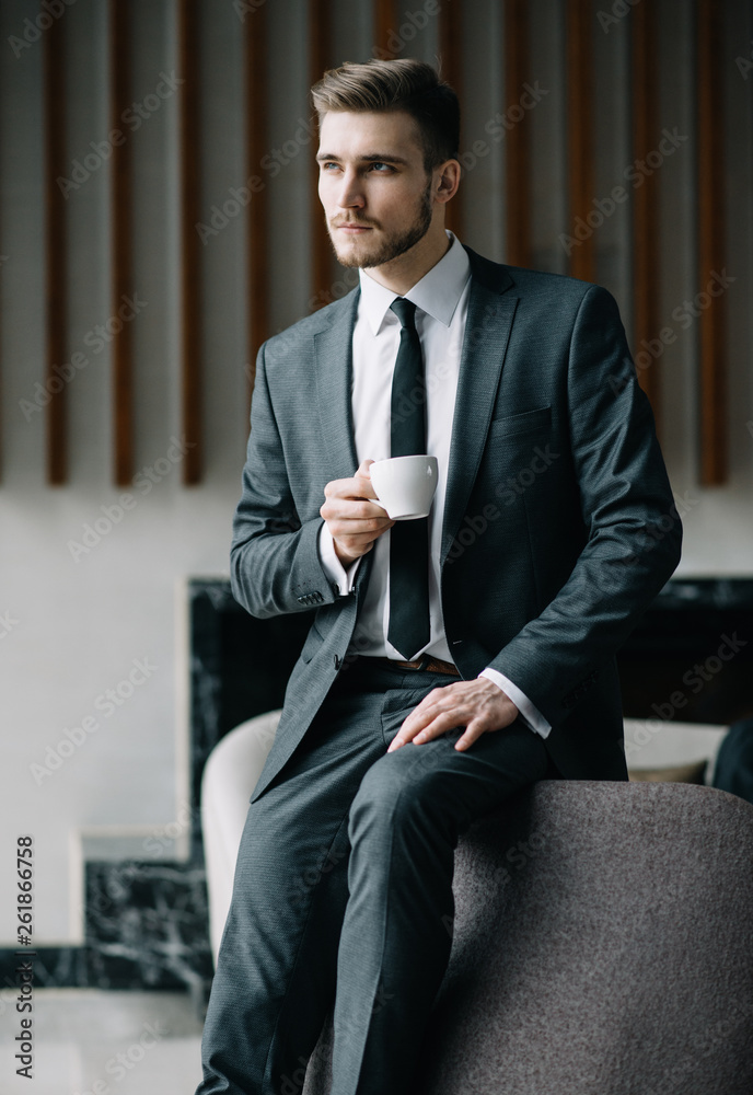 Young handsome man sitting in office with cup of coffee and working on project connected with modern cyber technologies. Businessman with notebook trying to keep deadline in digital marketing sphere. Young handsome man sitting in office with cup of coffee and working on project connected with modern cyber technologies. Businessman with notebook trying to keep deadline in digital marketing sphere.