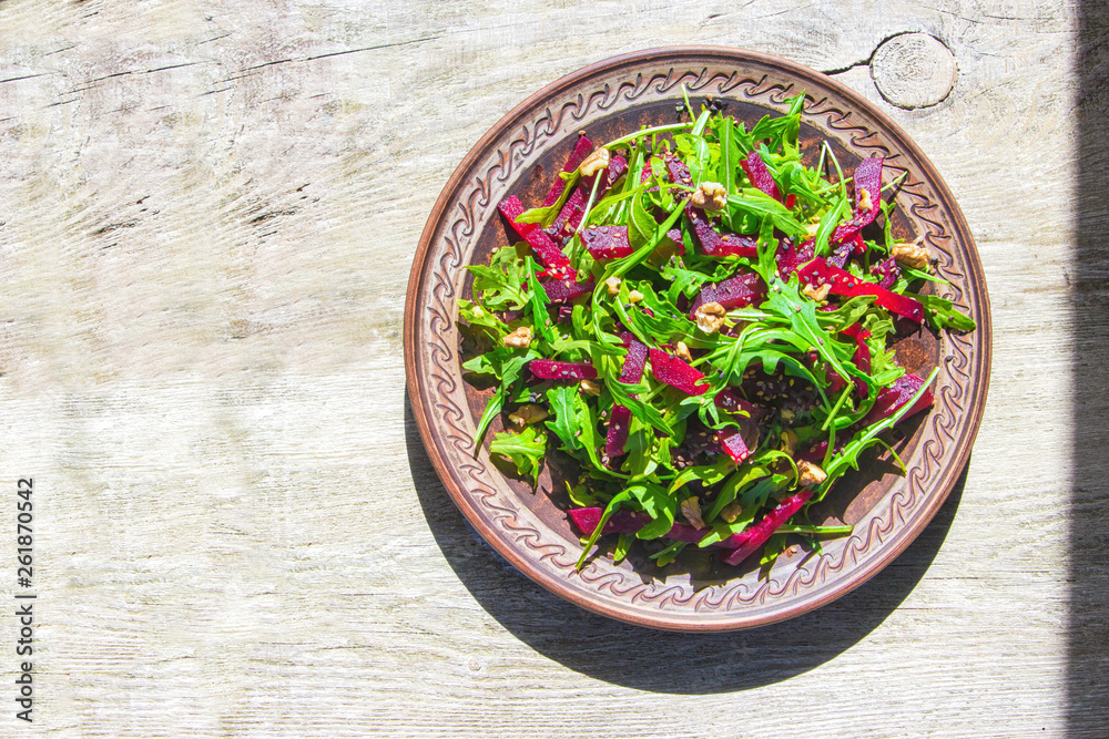 Spring detox salad salad with arugula and boiled beets with walnut kernel and roasted sesame seeds, poured with olive oil in a rustic ceramic plate on a wooden background, top view Spring detox salad salad with arugula and boiled beets with walnut kernel and roasted sesame seeds, poured with olive oil in a rustic ceramic plate on a wooden background, top view