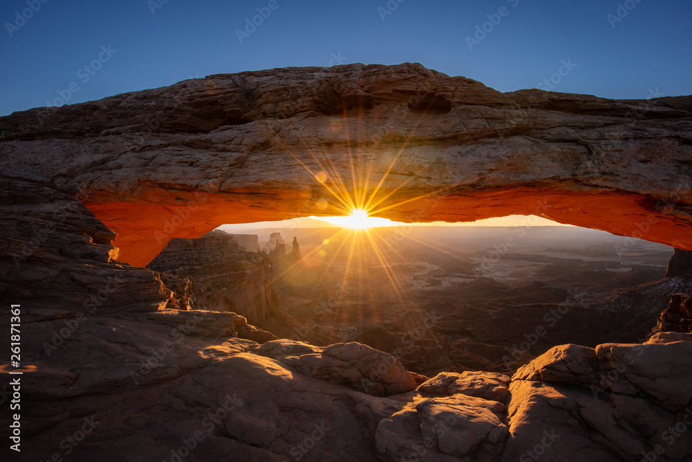 Mesa arch in Canyonlands National Park just outside Moab Utah. The sun beams like a sunstar through the window of the desert arch.  The cold snow contrasts the orange glow.