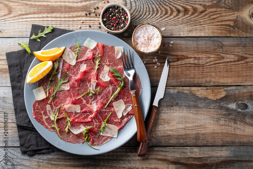 Photos Marbled beef carpaccio with arugula, lemon and parmesan cheese on wooden table