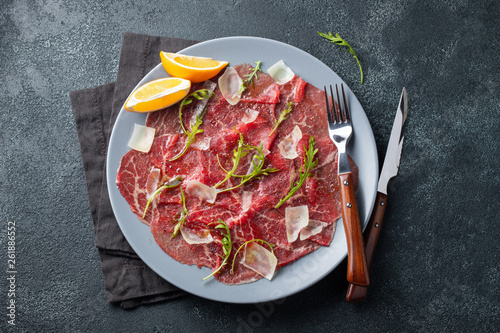 Marbled beef carpaccio with arugula, lemon and parmesan cheese on dark concrete table. Top view, flat lay