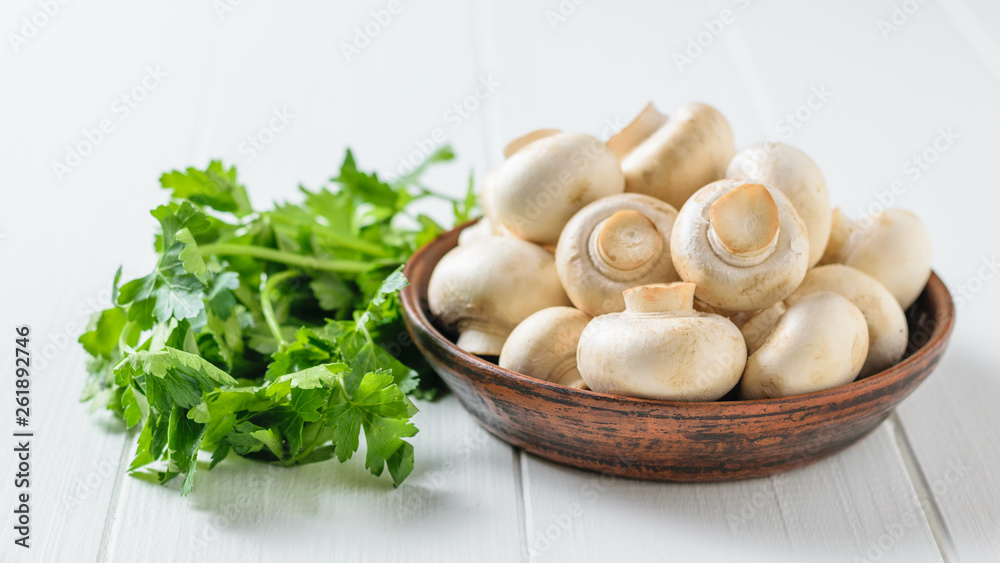 Mushrooms in a bowl with parsley leaves on a white wooden table. Vegetarian cuisine. Mushrooms in a bowl with parsley leaves on a white wooden table. Vegetarian cuisine.