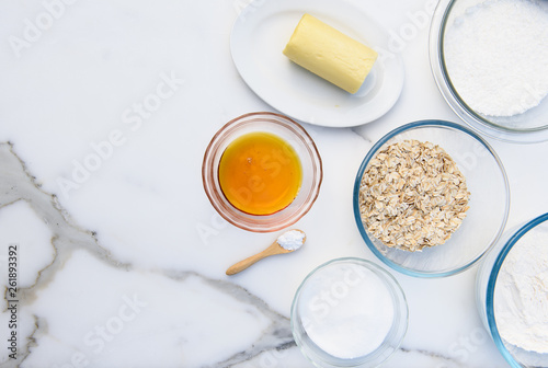 Ingredients for Anzac biscuits a traditional Australian cookie made with butter, desiccated coconut, sugar, golden syrup, rolled oats, baking soda and flour. Flat lay with copy space on marble bench 