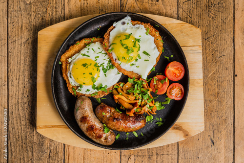 Traditional potato pancakes with fried eggs, mushrooms, sausages and tomatoes served on a hot frying pan.