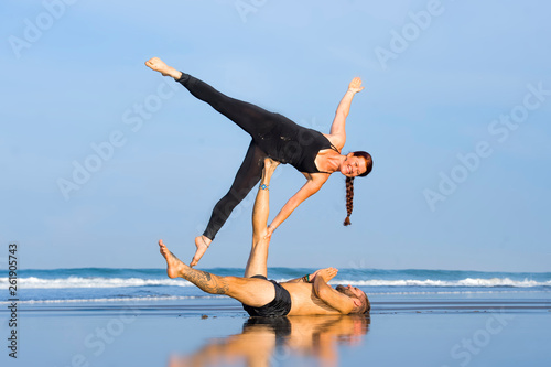 young attractive and beautiful acrobat couple practicing acroyoga exercise concentrated keeping balance practiing yoga on the beach in relaxation and meditation concept