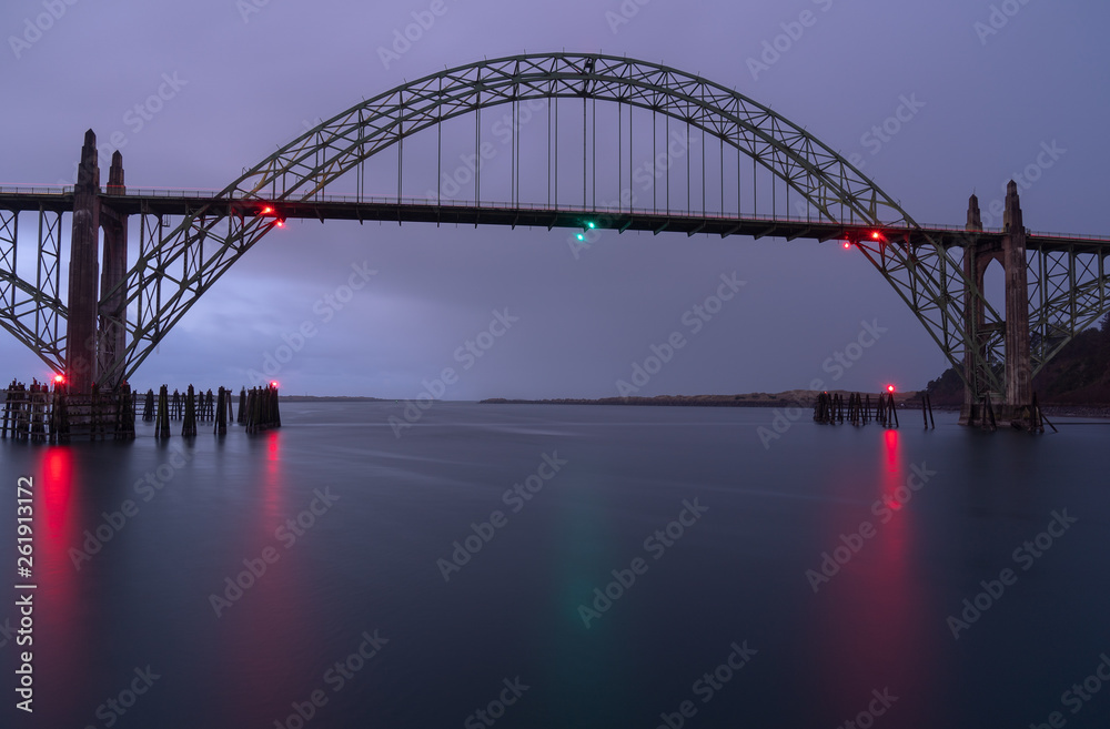 Fototapeta premium Moody metal bridge with colorful reflections on the river surface before sunrise in Newport, Oregon 
