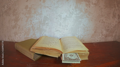 Old books lie on a bright brown table. Opened old book. Bookmarks banknotes in one dollar. Background old concrete wall.