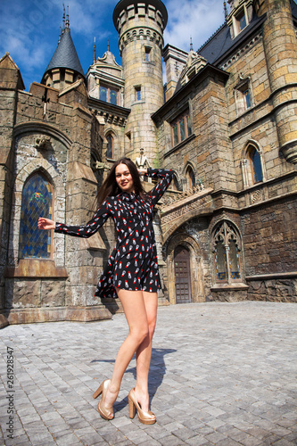 Full-length portrait young beautiful girl in summer dress posing against the backdrop of an old castle in the Gothic style © Andrey_Arkusha