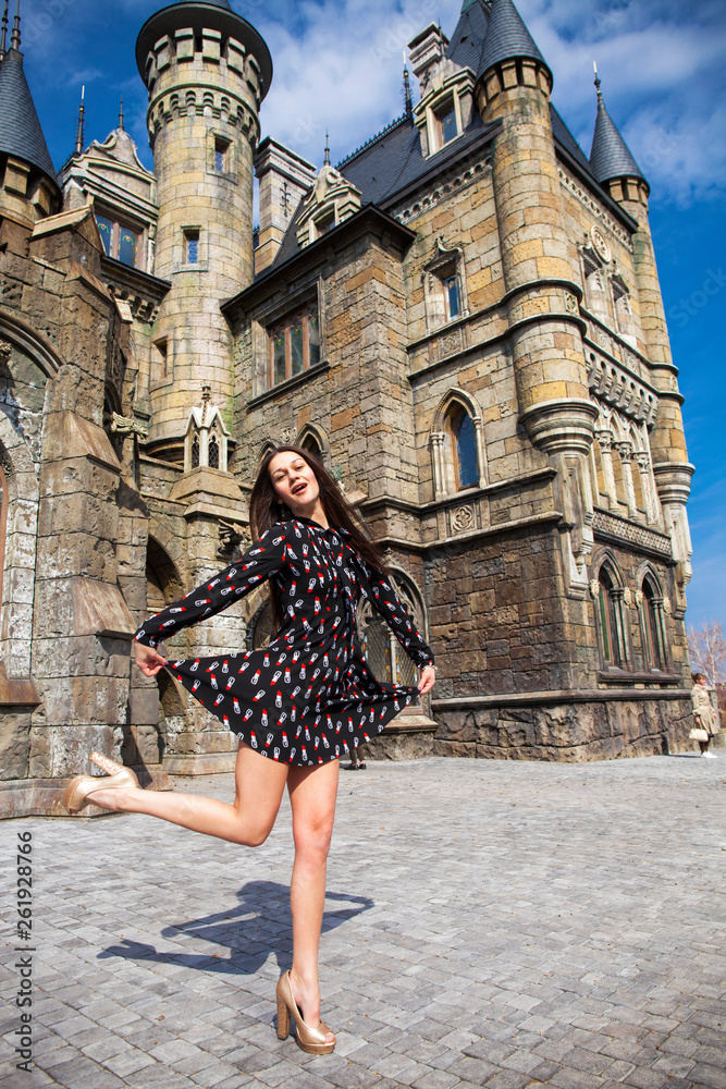 Full-length portrait young beautiful girl in summer dress posing against the backdrop of an old castle in the Gothic style