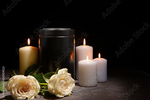Mortuary urn, burning candles and flowers on table against dark background