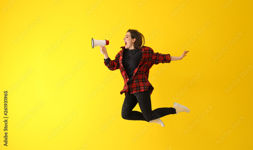 Fototapeta premium Jumping young woman with megaphone against color background