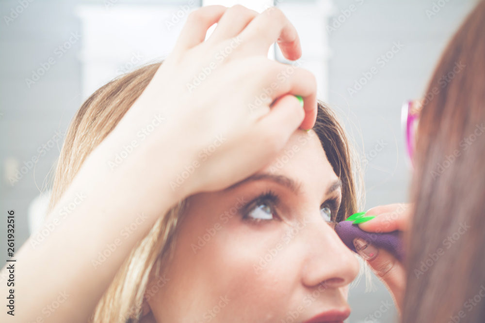 Naklejka premium Young blonde woman applying makeup to model in salon, beauty and fashion concept