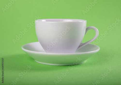 White mug and saucer on a green background.