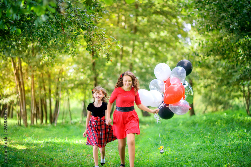 Fototapeta premium Two girls sit on the grass in the evening park with air balloons, happy kids concept