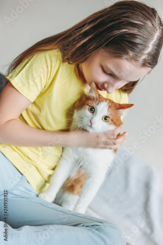 Fototapeta Naklejka Na Ścianę i Meble -  Cute tween girl in yellow t-shirt with her white cat at home