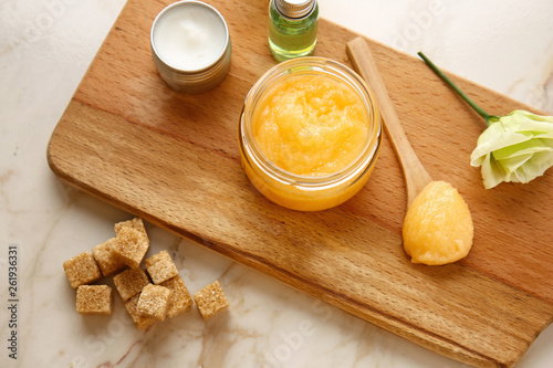 Jar with sugar scrub and cosmetic products on light table