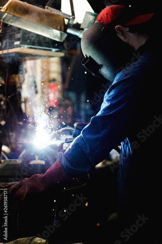 welder is welding metal part in garage. with protective mask, industrial steel welder