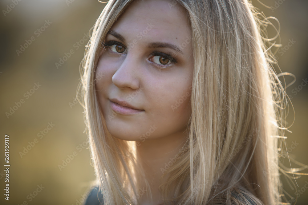 Young blonde girl in the evening soft light of the sun. Large portrait of a girl with long hair, hair blown by the wind.