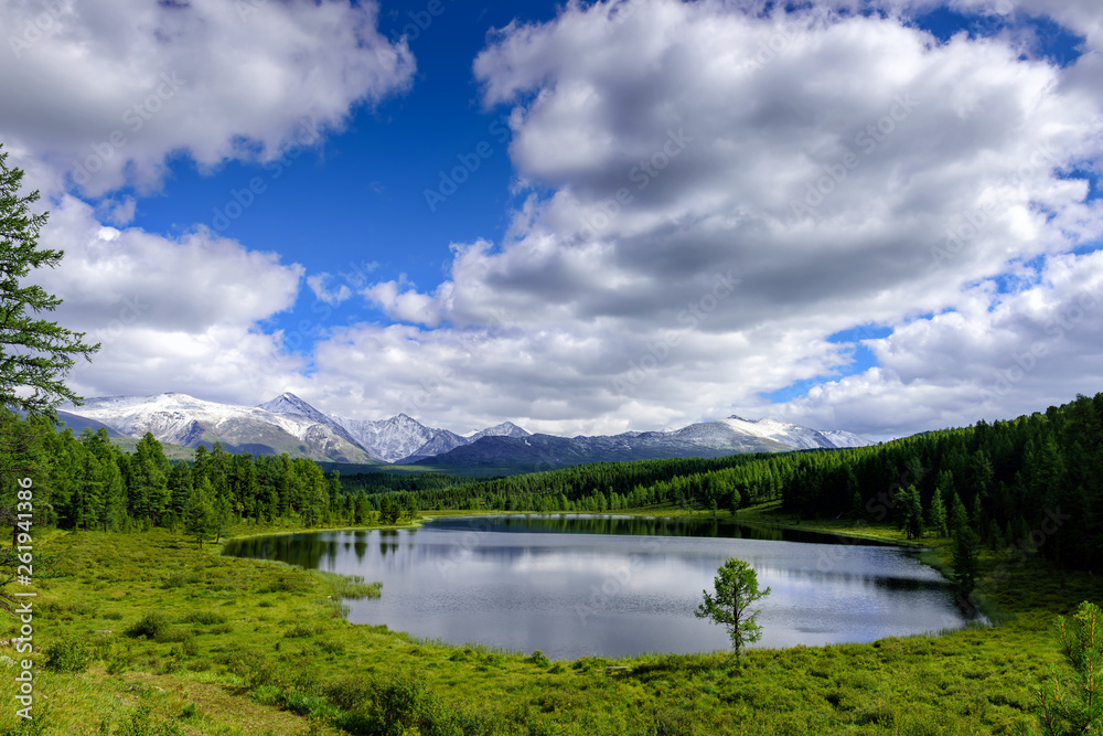 Mountain landscape, white clouds, lake and mountain range in the distance. Fantastic sunny day in mountains, large panorama. Location is in Altai, Russia.