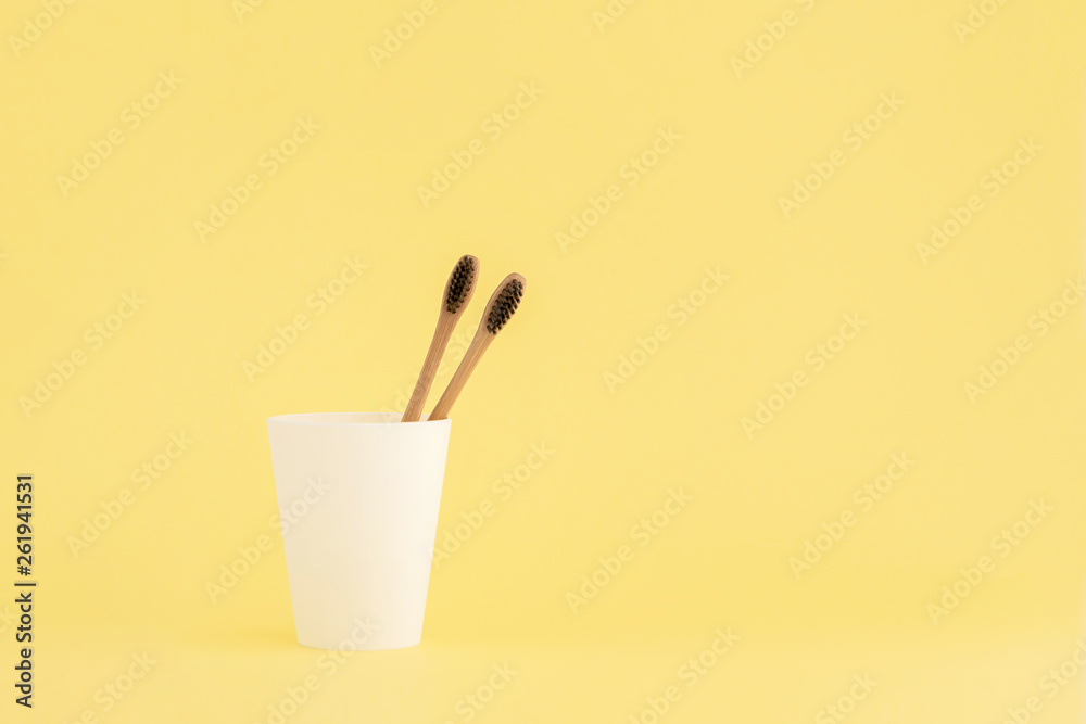 Two wooden toothbrushes in cup on yellow background.