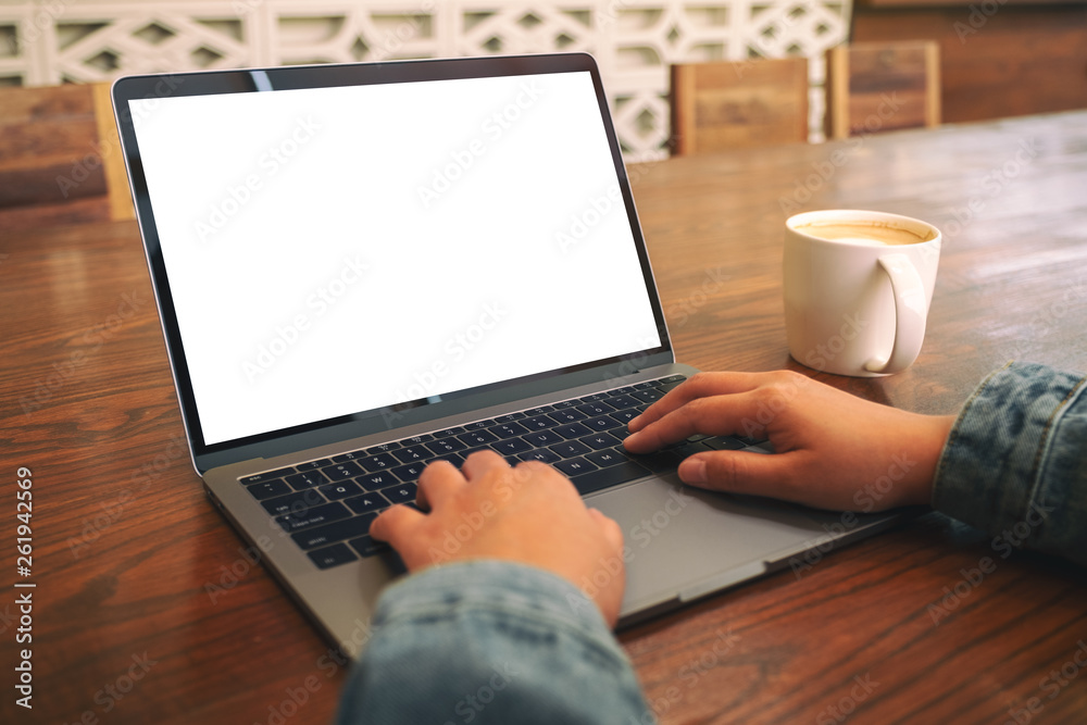 Fototapeta premium Mockup image of a woman using and typing on laptop with blank white screen and coffee cup on wooden table