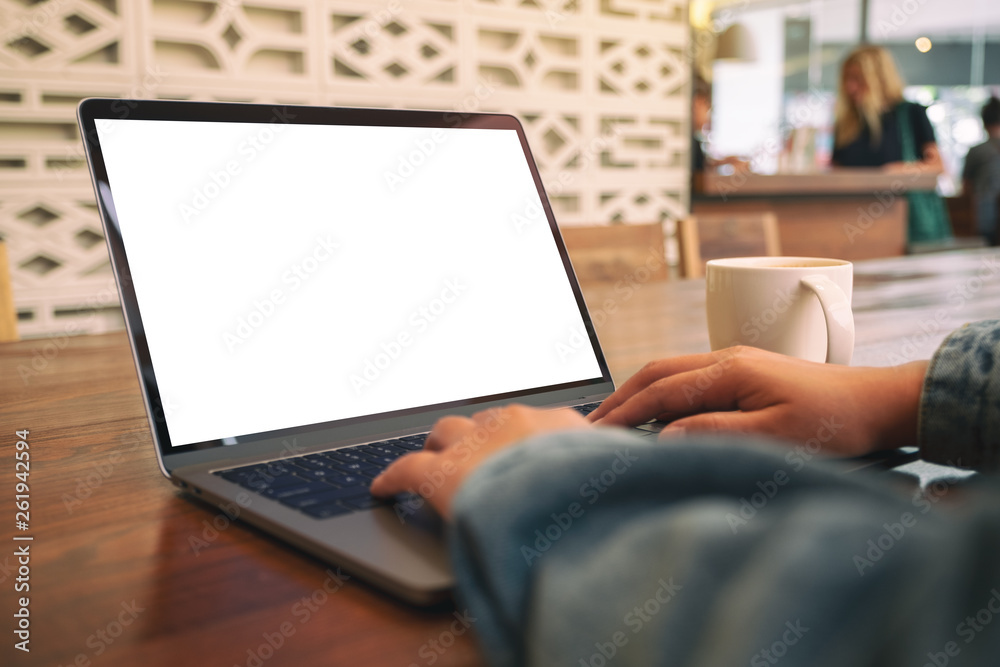 Mockup image of a woman using and typing on laptop with blank white screen and coffee cup on wooden table Mockup image of a woman using and typing on laptop with blank white screen and coffee cup on wooden table