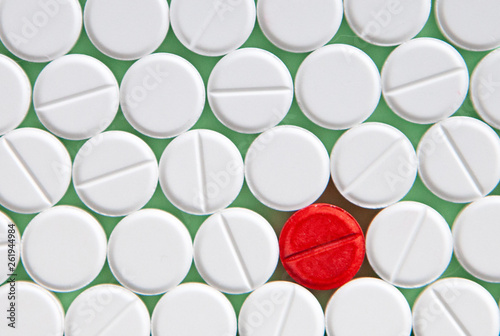 Top view of a pile of white medicine pills on a white surface. One tablet of red medication. Vaccine concept