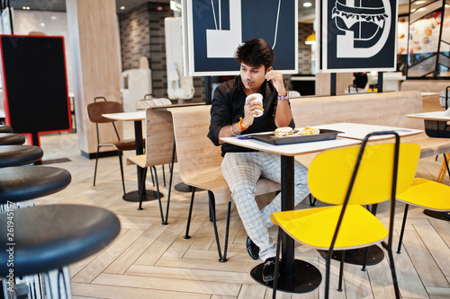 Stylish indian man sitting at fast food cafe and drink soda.