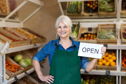 Senior woman holding open sign in organic produce shop