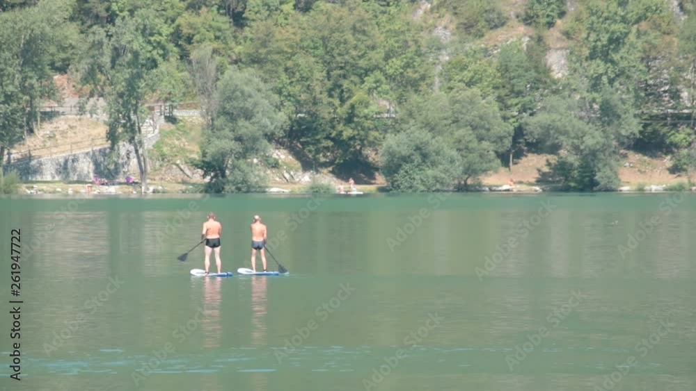 Row On Surfing Board. Two Men On A Stand Up Paddle Board Rows On A Quiet Lake Row On Surfing Board. Two Men On A Stand Up Paddle Board Rows On A Quiet Lake