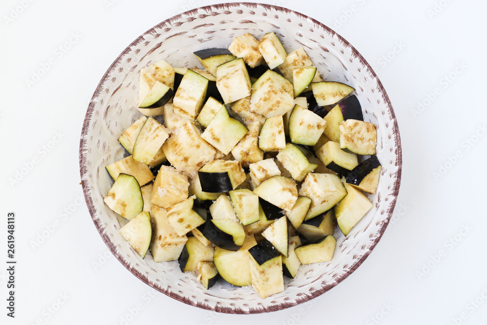 Eggplant cut into cubes for salad, placed in a plate on a white background, top view