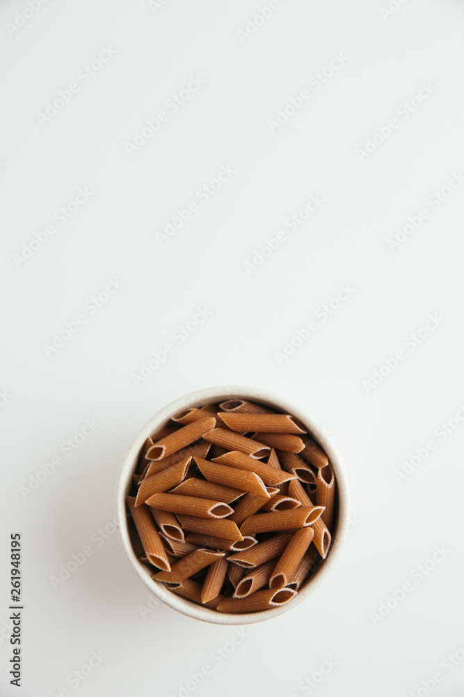 Whole grain macaroni on white background, vertical, free space for text, top view