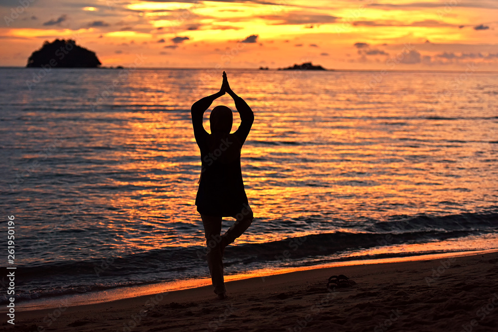 Girl in silhouette doing yoga on the beach at sunset