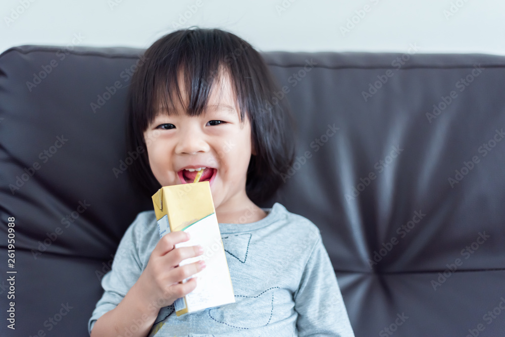Happy Sweet Asian baby child drinking a carton of milk from box with straw on sofa Happy Sweet Asian baby child drinking a carton of milk from box with straw on sofa