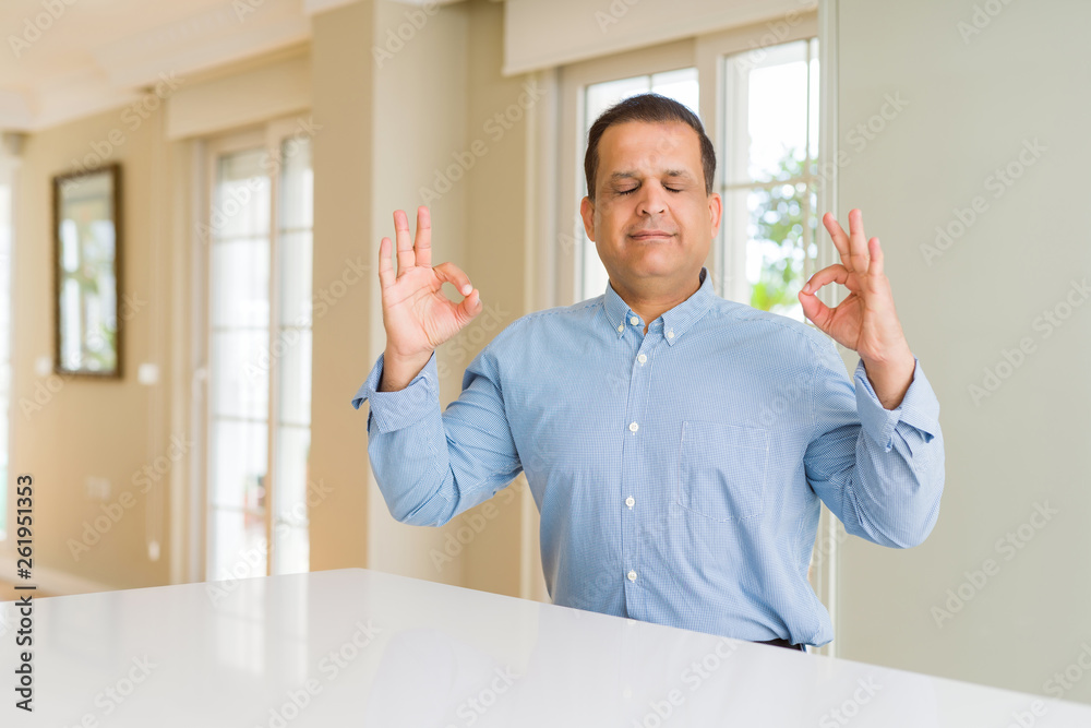 Middle age man sitting at home relax and smiling with eyes closed doing meditation gesture with fingers. Yoga concept.